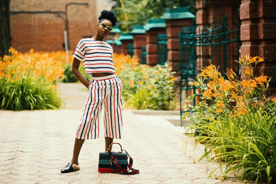 summer fashion trends - A stylish woman posing in a garden wearing a striped outfit with accessories.